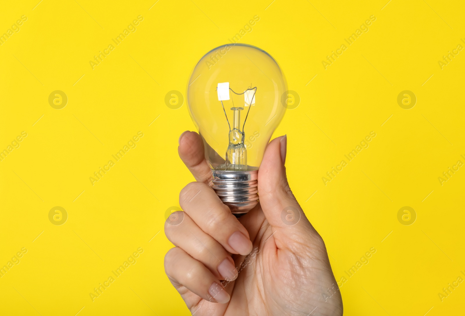 Photo of Woman holding incandescent light bulb on yellow background, closeup