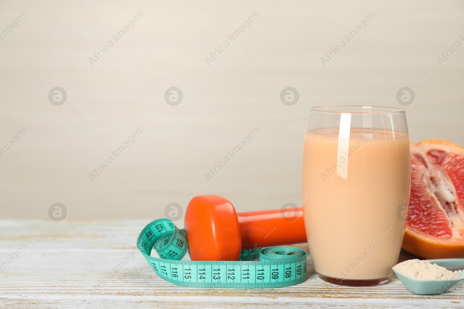 Photo of Tasty shake with grapefruit, dumbbell, measuring tape and powder on wooden table against light background, space for text. Weight loss