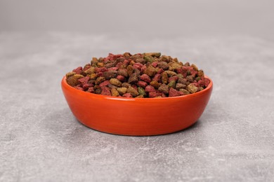 Photo of Dry food in orange pet bowl on grey surface