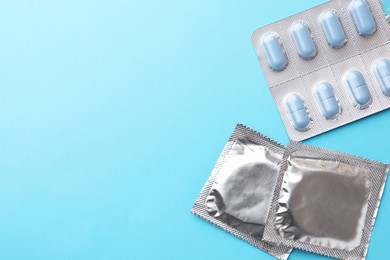 Photo of Pills and condoms on light blue background, flat lay with space for text. Potency problem