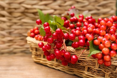 Photo of Wicker basket with ripe red viburnum berries on wooden table, closeup