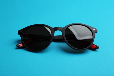 Photo of Stylish sunglasses on blue background. Fashionable accessory