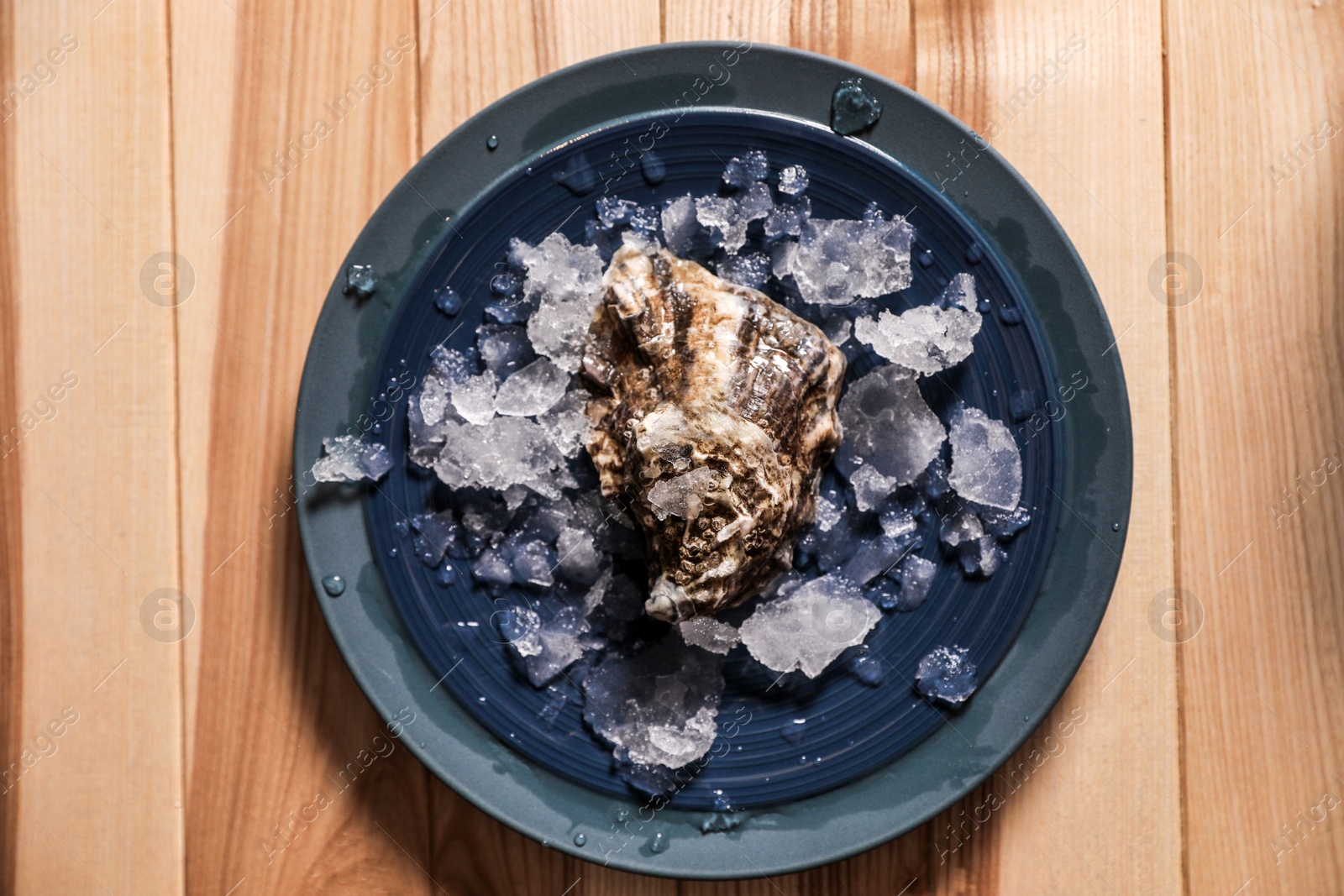 Photo of Fresh oyster with ice on wooden table, top view