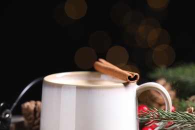 Tasty eggnog with cinnamon stick against blurred lights, closeup