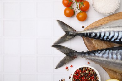 Photo of Raw mackerel, tomatoes and peppercorns on white tiled table, flat lay. Space for text