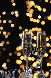 Glasses of champagne and serpentine streamers against black background with blurred lights. Space for text