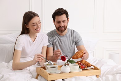 Photo of Happy couple eating tasty breakfast in bed at home