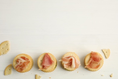 Delicious crackers with prosciutto on white wooden table, flat lay. Space for text