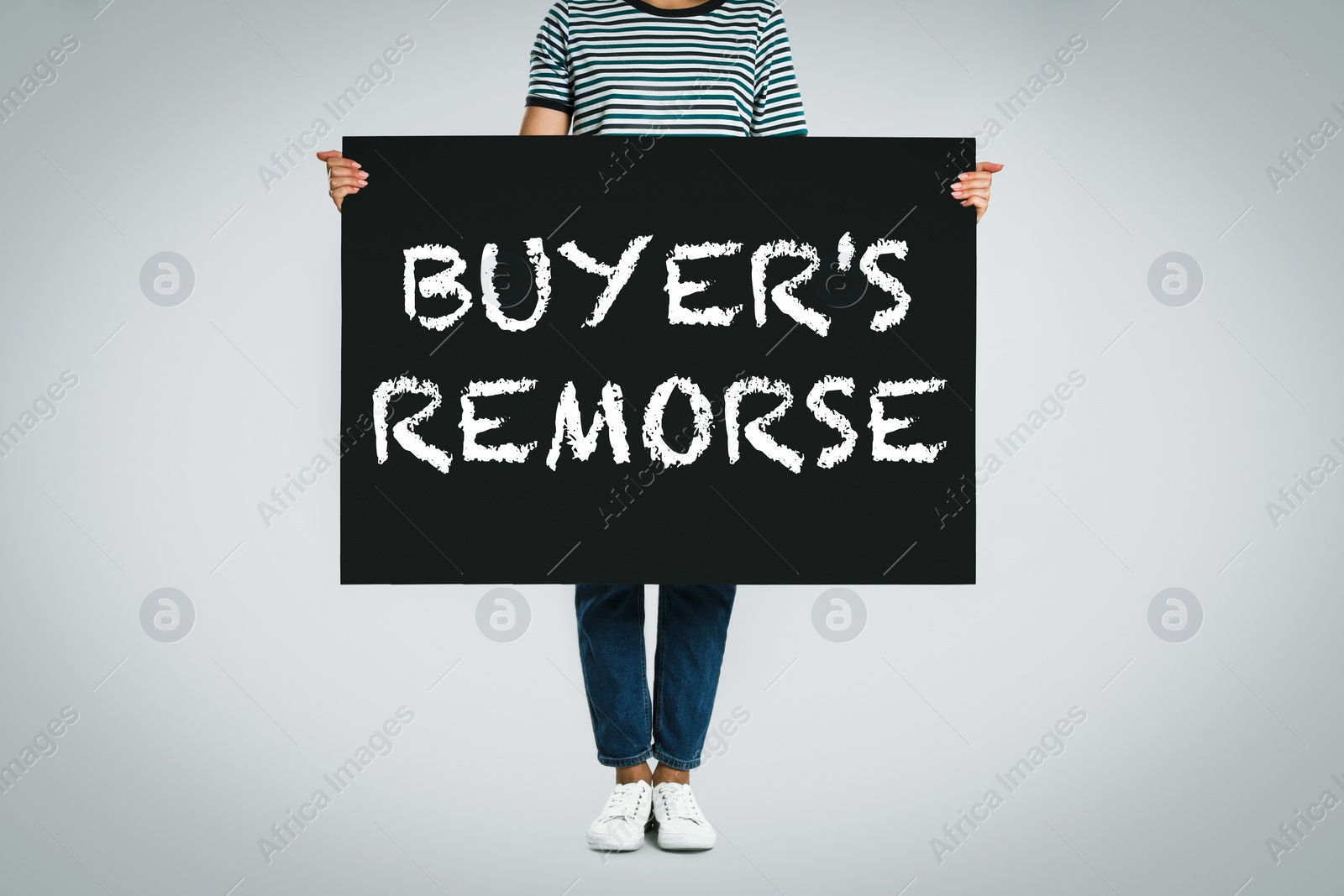 Image of Woman holding poster with text Buyer's Remorse on light grey background, closeup