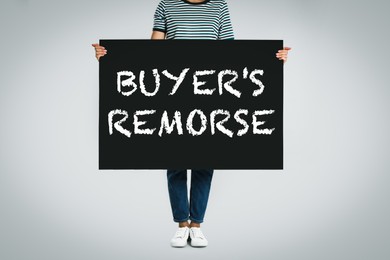 Image of Woman holding poster with text Buyer's Remorse on light grey background, closeup