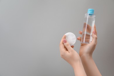 Photo of Woman holding makeup remover and cotton pad on light grey background, closeup. Space for text