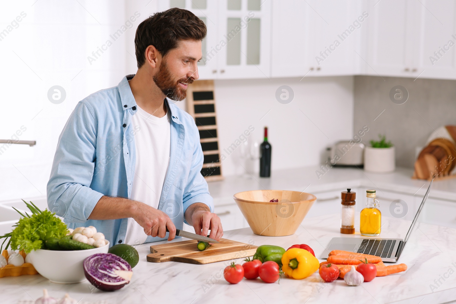 Photo of Man making dinner while watching online cooking course via laptop in kitchen