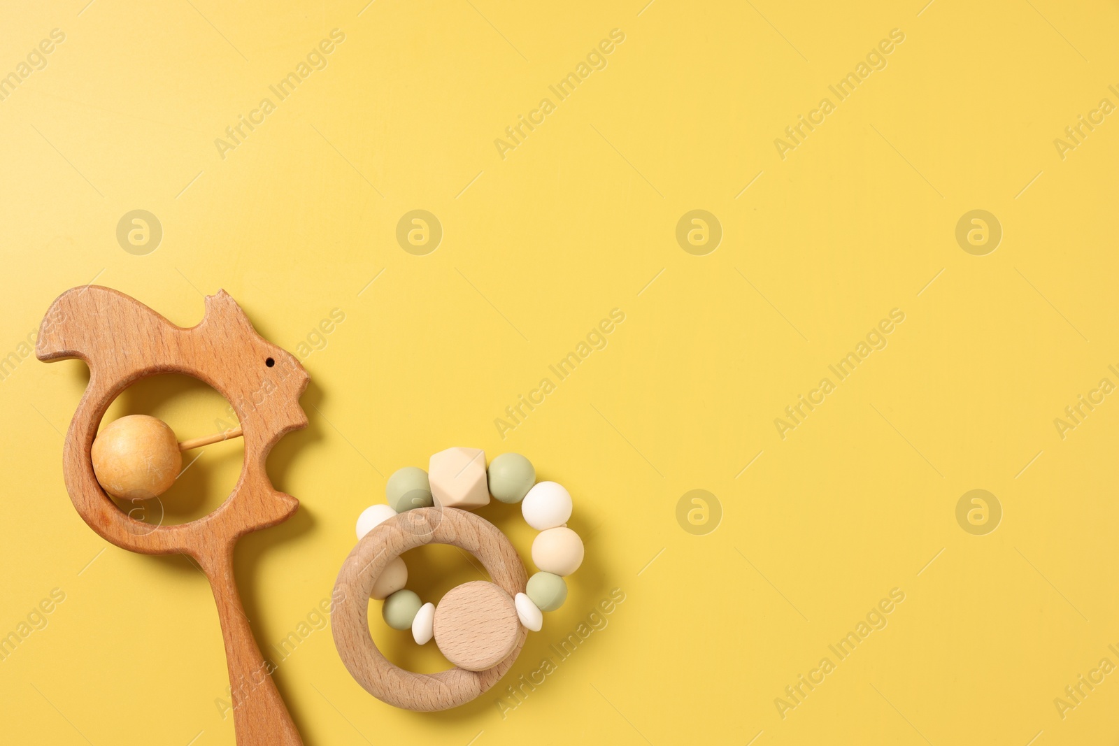 Photo of Baby accessories. Wooden rattles on yellow background, top view. Space for text