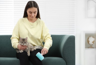 Photo of Pet shedding. Woman with lint roller removing cat`s hair from trousers on sofa at home, space for text
