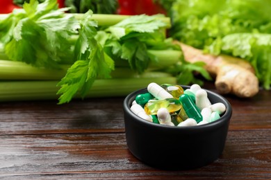 Dietary supplements. Pills in bowl and food products on wooden table, closeup