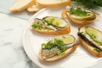 Photo of Delicious sandwiches with sprats, pickled cucumber, green onion and dill on white marble table, closeup. Space for text