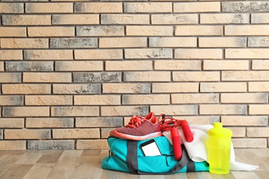 Photo of Sports bag and gym equipment on wooden floor near brick wall