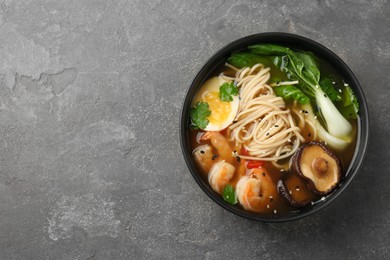 Photo of Delicious ramen with shrimps and egg in bowl on grey textured table, top with space for text. Noodle soup