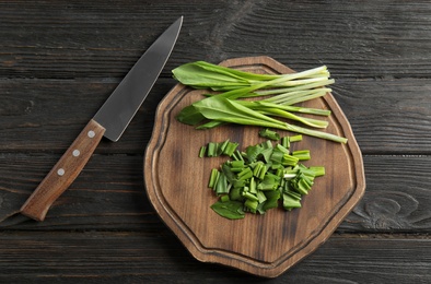 Board with wild garlic or ramson and knife on wooden table, flat lay