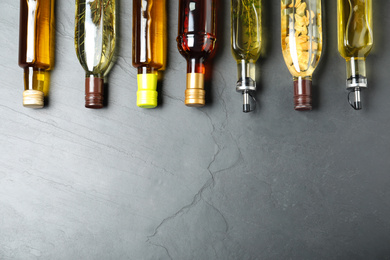 Photo of Different sorts of cooking oil in bottles on grey table, flat lay. Space for text