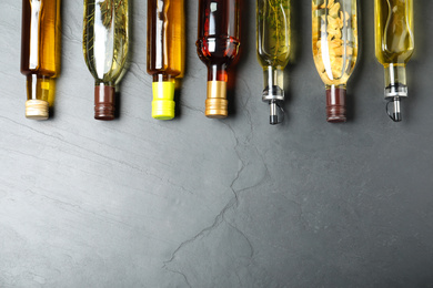 Different sorts of cooking oil in bottles on grey table, flat lay. Space for text