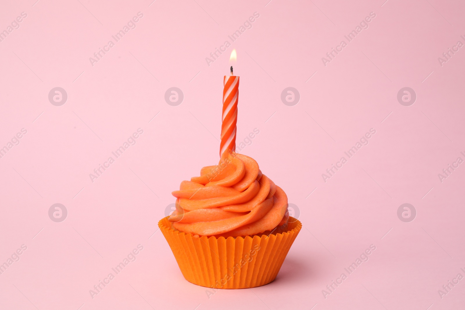 Photo of Delicious birthday cupcake with orange cream and burning candle on pink background