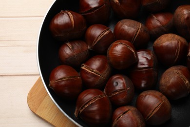 Roasted edible sweet chestnuts in frying pan on wooden table, top view