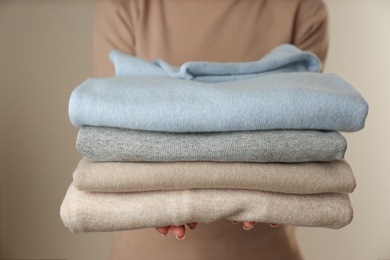 Woman with folded cashmere clothes on beige background, closeup