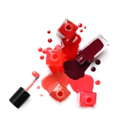 Spilled different nail polishes with bottles on white background, top view