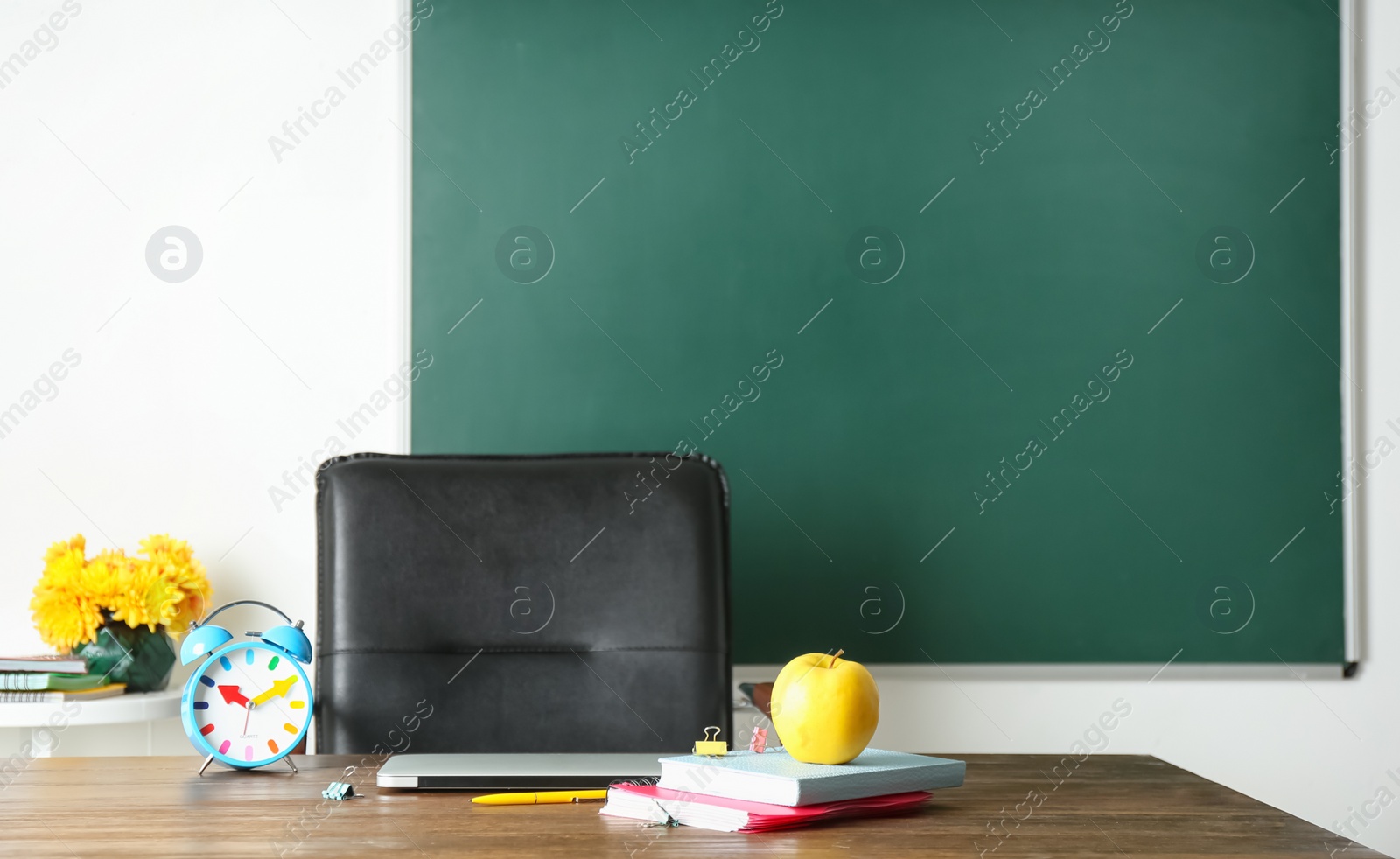 Photo of Laptop, notebooks and alarm clock on table in classroom. Teacher day celebration