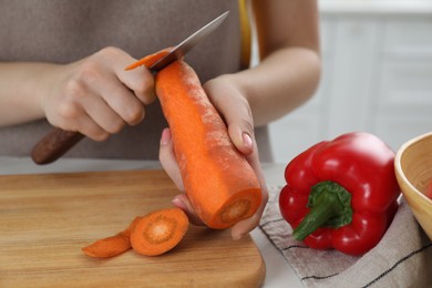 Photo of Woman peeling fresh carrot with knife at white marble table indoors, closeup