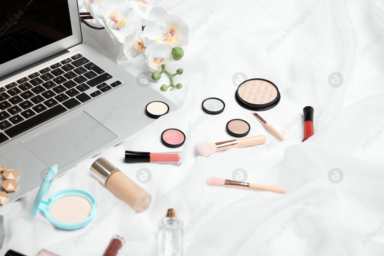 Photo of Composition with laptop and makeup products for woman on bed