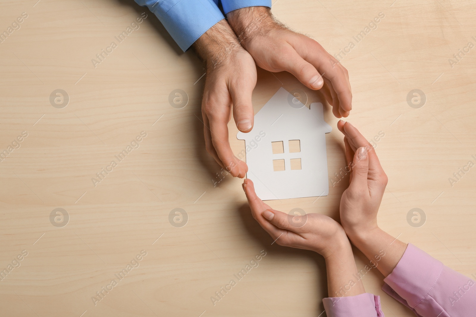 Photo of Couple holding hands near paper silhouette of house on wooden background, top view with space for text. Home insurance