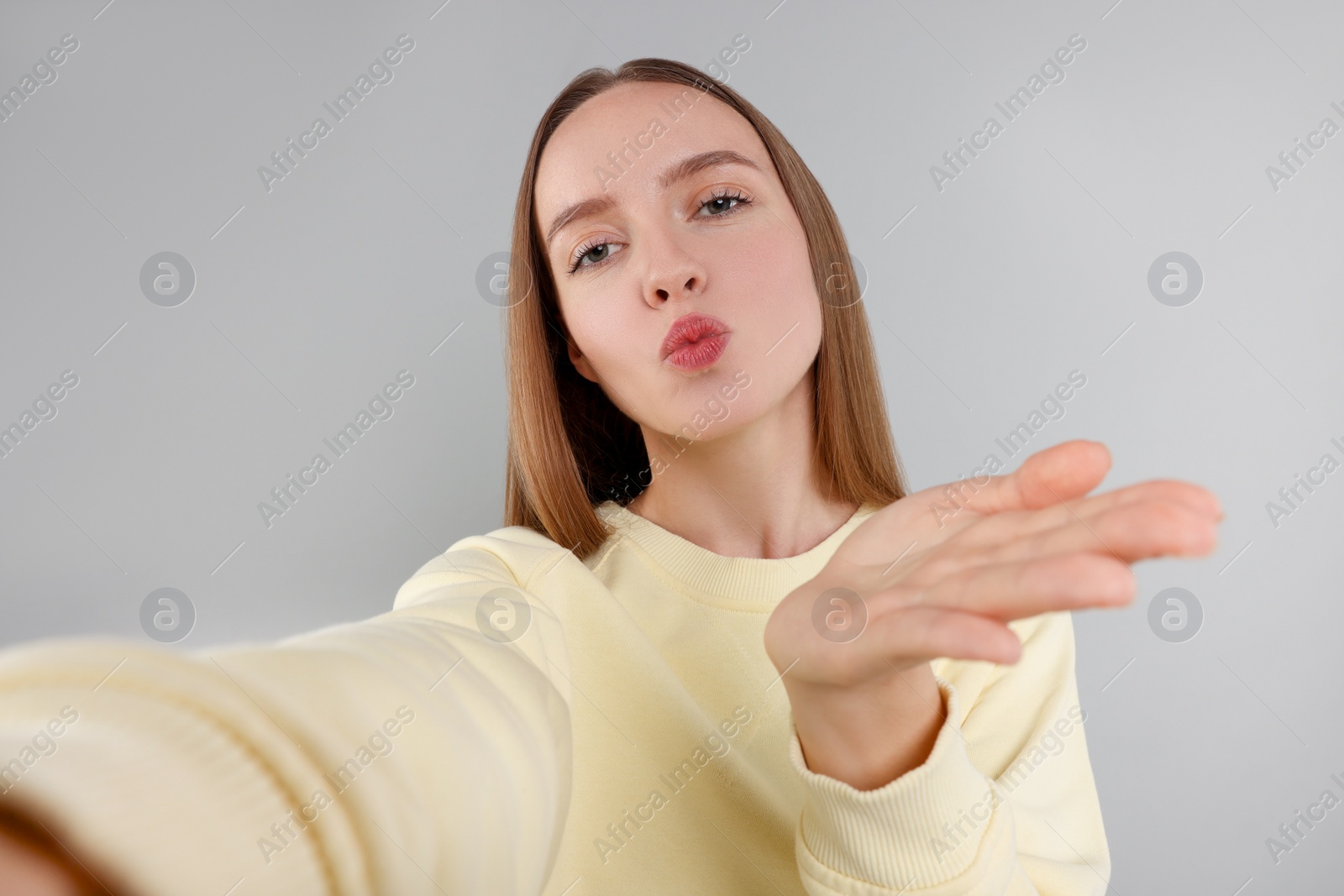 Photo of Young woman taking selfie and blowing kiss on light grey background