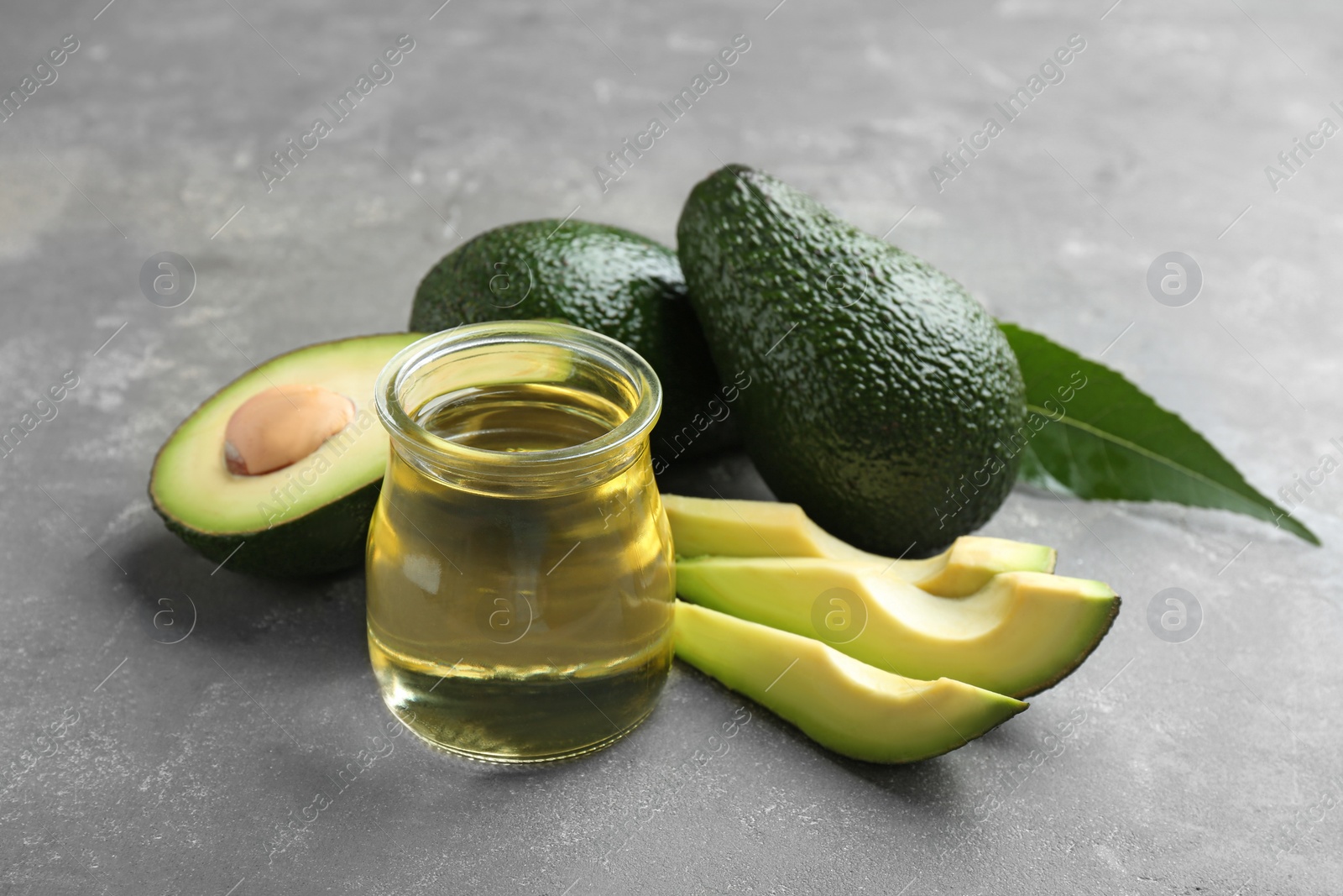 Photo of Jar of natural oil and avocados on grey stone background