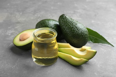 Photo of Jar of natural oil and avocados on grey stone background