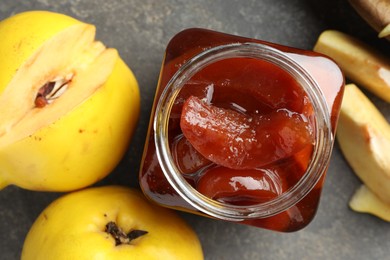 Tasty homemade quince jam in jar and fruits on grey textured table, flat lay