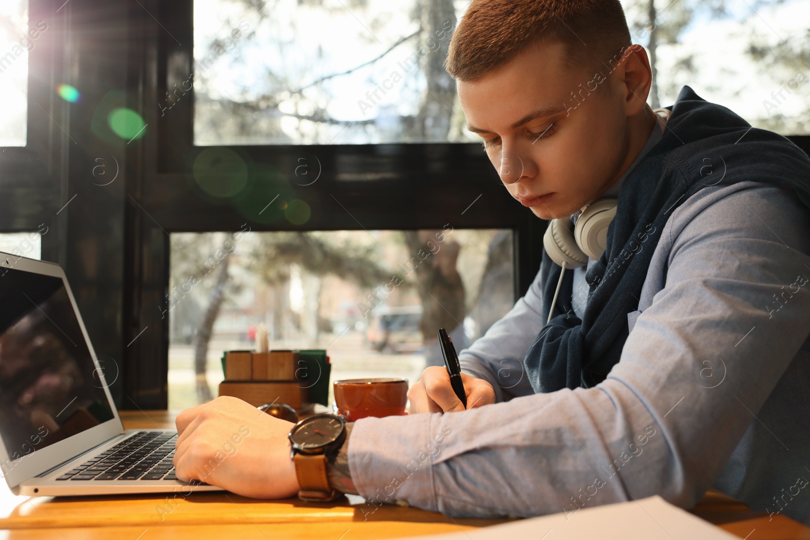 Photo of Young male student with laptop studying at table in cafe