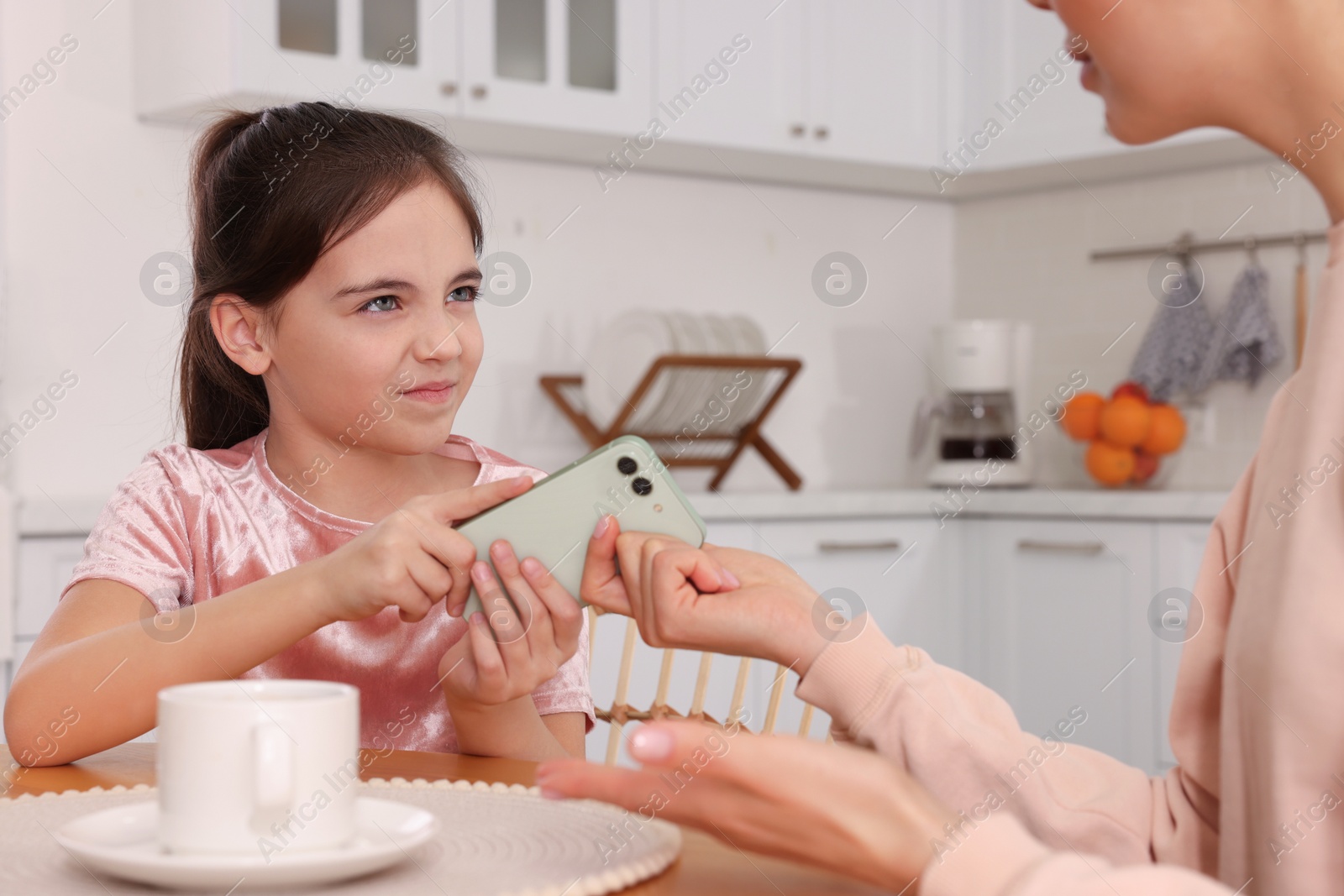 Photo of Internet addiction. Woman taking smartphone from her angry daughter in kitchen