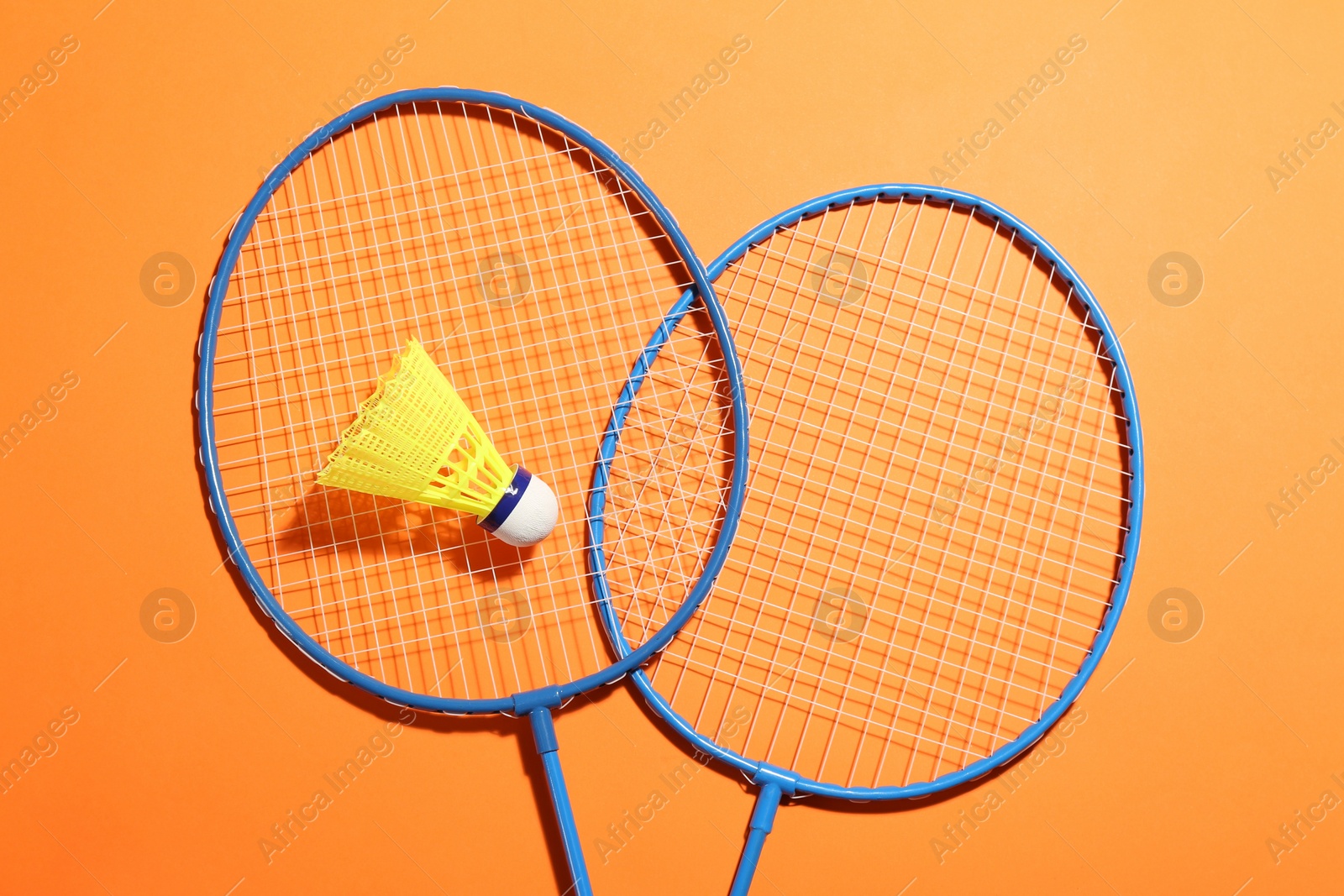 Photo of Badminton rackets and shuttlecock on orange background, flat lay. Space for text