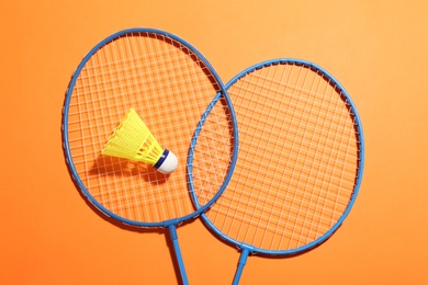 Badminton rackets and shuttlecock on orange background, flat lay. Space for text
