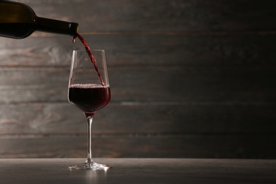 Photo of Pouring red wine into glass from bottle on table against wooden background. Space for text