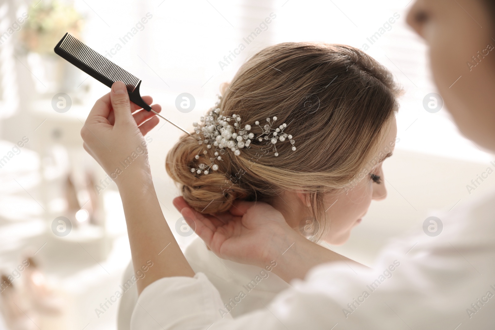 Photo of Professional stylist making wedding hairstyle for bride in salon