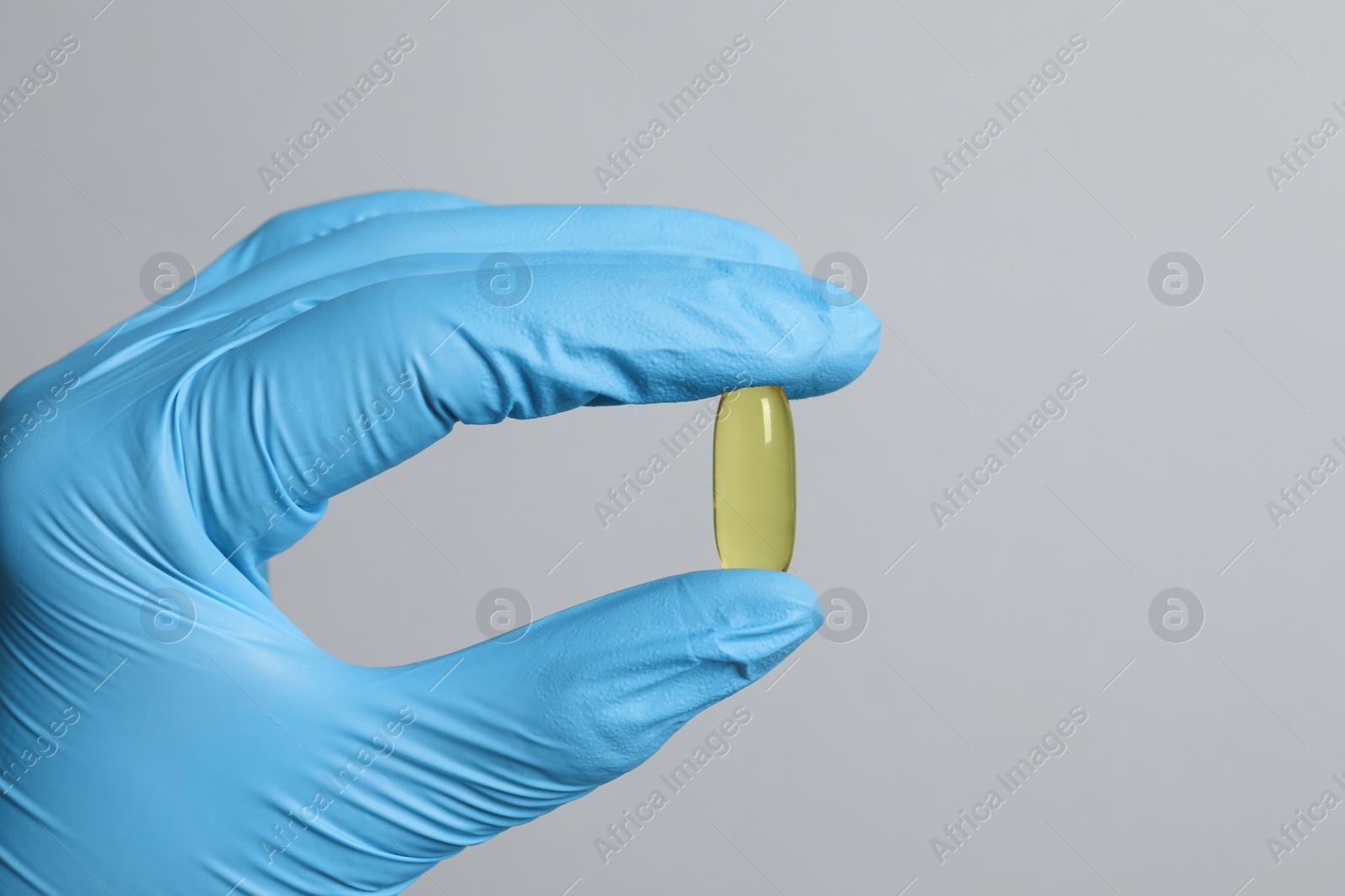 Photo of Doctor holding pill on grey background, closeup. Space for text