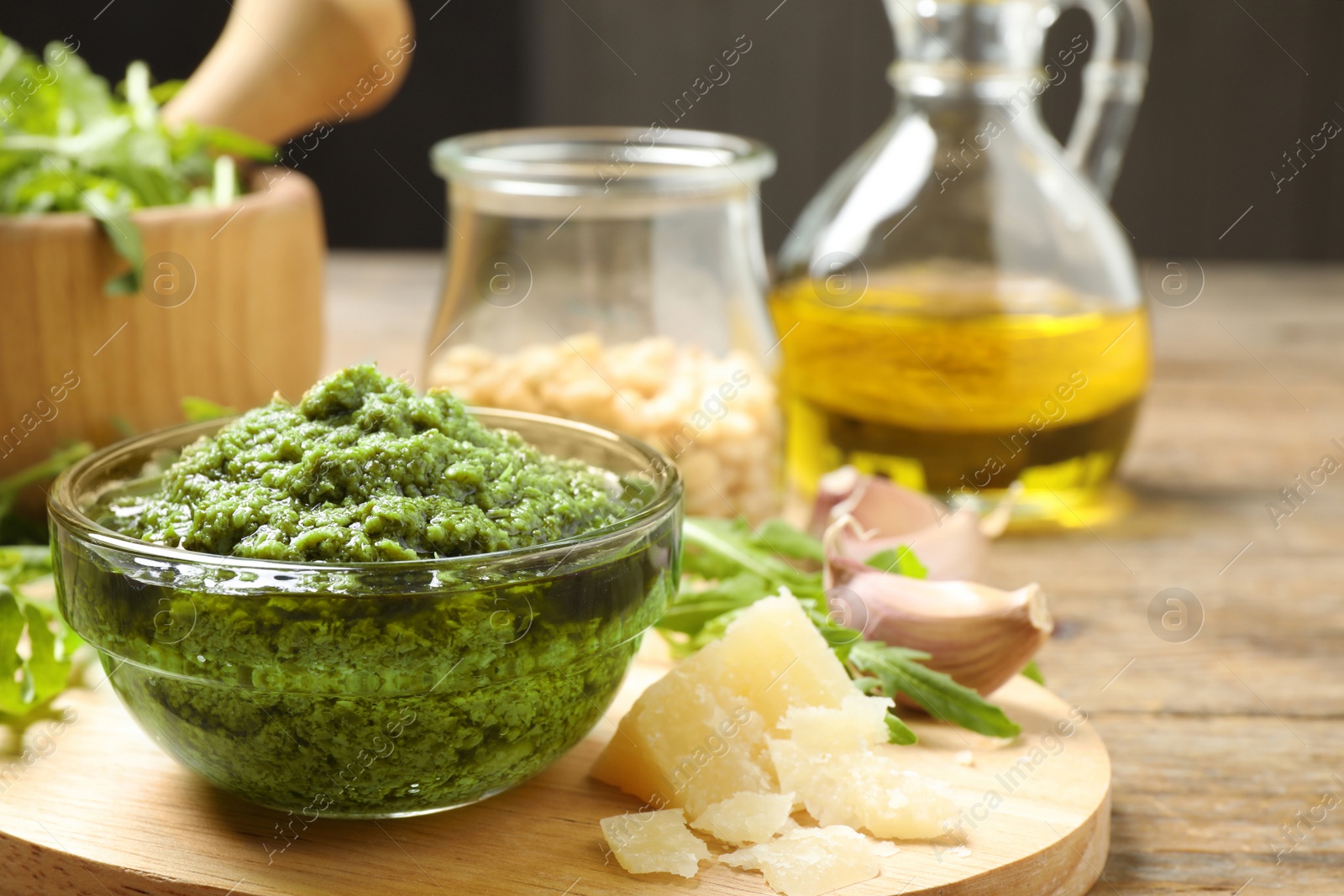 Photo of Bowl of tasty arugula pesto and ingredients on table, closeup