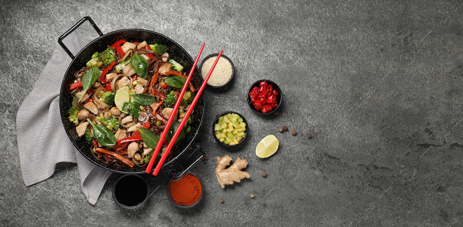 Photo of Stir-fry. Tasty noodles with meat in wok, chopsticks and ingredients on grey textured table, flat lay. Space for text