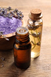 Photo of Bowl of sea salt, essential oil and lavender flowers on wooden table, closeup