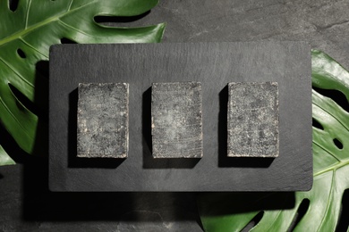 Natural tar soap on black table with green leaves, flat lay