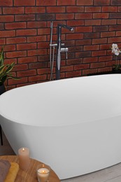 Stylish bathroom interior with ceramic tub, burning candles and terry towels on wooden table