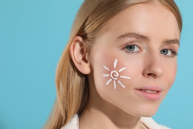 Beautiful young woman with sun protection cream on her face against light blue background, closeup. Space for text